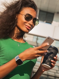 A pretty black woman with a takeaway coffee in her hand and her iphone in the other hand.