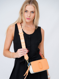 A lady modelling a peach sling bag with a patterned strap.