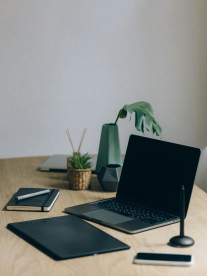 A black laptop and note pad on a wooden scandinavian desk.